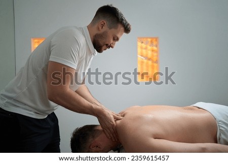 Qualified masseur giving upper back trigger point massage to patient Royalty-Free Stock Photo #2359615457