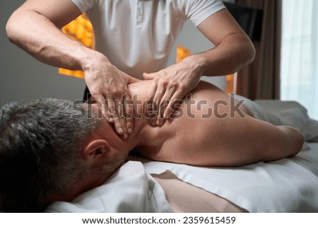 Masseur giving upper back massage to client