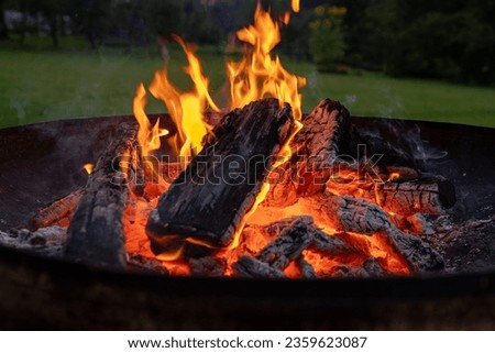 Vivid smoldered firewoods burned in fire close-up. Atmospheric background with orange flame of campfire and smoke. Warm full frame image of bonfire. Glowing embers in air. Sunset. Selective focus.