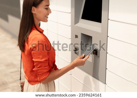 Young European Woman Withdrawing Money At Atm Machine, Using Mobile Phone Like Bank Credit Card Standing In Urban City Area Outdoors. Currency And Easy Financial Transactions Via Cellphone. Cropped