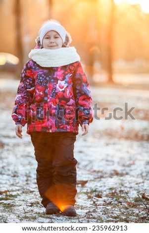 Girl on a walk in winter park in the rays of the setting sun, looking at the camera