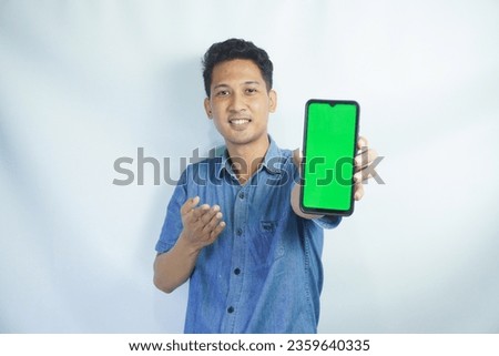 Portrait of a Asian man holding a big green screen smartphone in his hand, showing and pointing at the device, banner