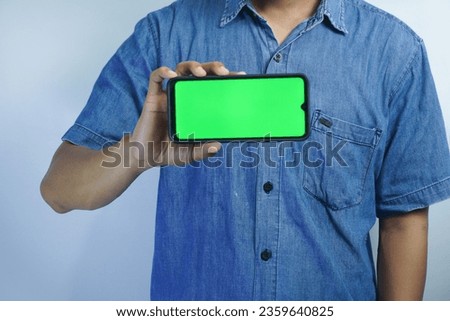 Portrait of a Asian man holding a big green screen smartphone in his hand, showing and pointing at the device, banner