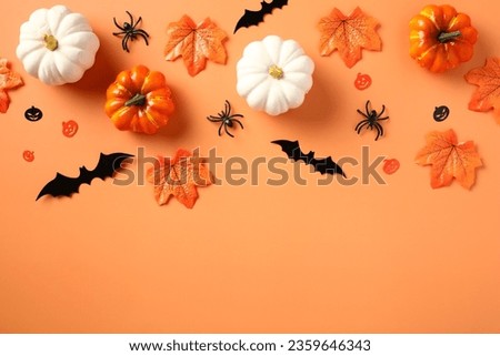 Halloween flat lay composition with pumpkins, spiders, bats, maple leaves on pastel orange background.
