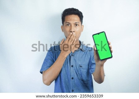  Portrait of a Asian man holding a big green screen smartphone in his hand, showing and pointing at the device, banner