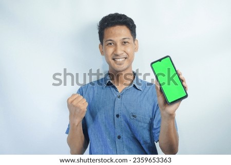  Portrait of a Asian man holding a big green screen smartphone in his hand, showing and pointing at the device, banner