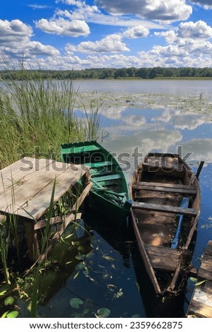 The photo was taken in Ukraine, on the river Southern Bug. The picture shows a fishing boat moored near the river bank under a blue sky with light clouds reflected in the water.