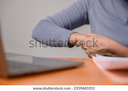 Close-up photo of an Asian business woman who has hand and wrist pain while using a laptop computer in the living room at home at a desk Office syndrome concept