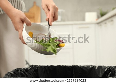 Woman throwing vegetable salad into bin indoors, closeup Royalty-Free Stock Photo #2359684023