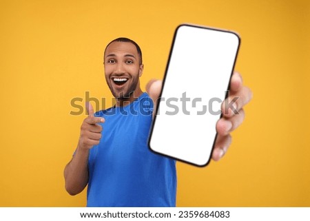 Young man showing smartphone in hand and pointing at it on yellow background Royalty-Free Stock Photo #2359684083