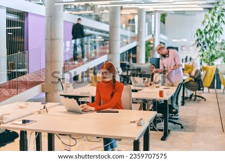 In a modern startup office, a professional businesswoman with orange hair sitting at her laptop, epitomizing innovation and productivity in her contemporary workspace. Royalty-Free Stock Photo #2359707575