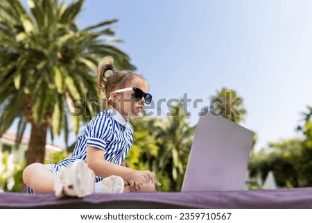 Young girl wearing sunglasses and looking at laptop screen. Swimming pool in the background. Tourist summer concept.