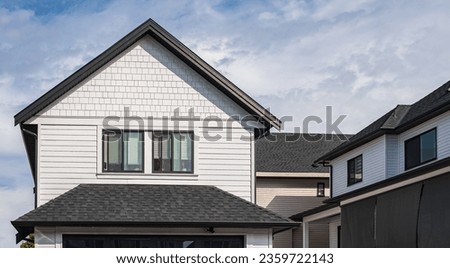 Houses with shingle roof against blue sky. Edge of roof shingles on top of the houses dark asphalt tiles on the roof. Nobody, street photo, selective focus Royalty-Free Stock Photo #2359722143