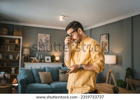 One man adult caucasian male with beard and eyeglasses stand at home happy smile use mobile phone smartphone to send sms text messages or browse internet online copy space Royalty-Free Stock Photo #2359733737