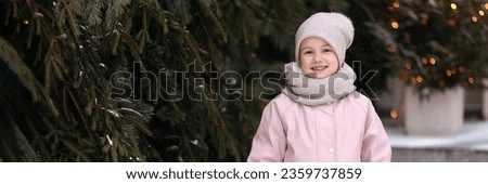 Girl in winter clothes on the background of Christmas trees and Garland lights. Girl on a decorated Christmas street. Banner on the theme of winter holidays.Banner for template design with copy space.