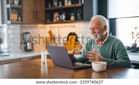 Cheerful senior man during video conference in kitchen on the laptop while enjoying breakfast and a cup of coffee. Elderly person using internet online chat technology video webcam making a video call