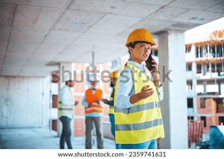 Caucasian businesswoman talk on phone while work. Gorgeous caucasian female architect in yellow west and with protective helmet on standing at construction site and using smart phone.