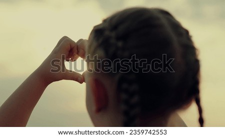 Hands shape heart. Little girl make sign love hands sunset. Small kid draw heart hands against sky. Sign heart symbol love, feeling. Silhouette of heart hands in sun close-up.Sunlight between fingers
