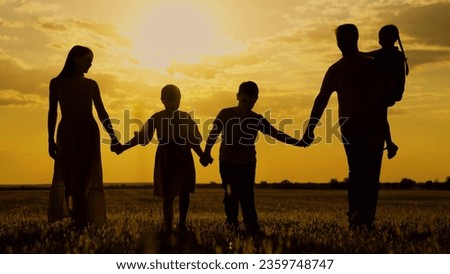 Active family with children walks in grass field in summer. Big family, group of people, nature. Silhouette family, Dad mom daughter son go hand in hand outdoors in autumn. Parental care for children