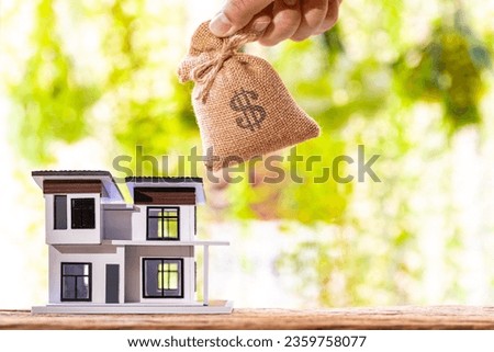 Loans for real estate concept, Man hand holding the money bag on the home model put on the wood in the public park.