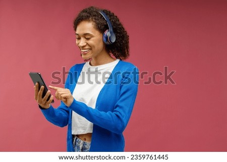 Smiling woman listen music in earphones standing on red studio background. High quality photo Royalty-Free Stock Photo #2359761445