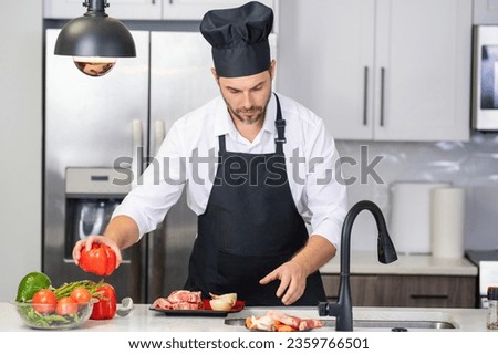 Handsome man is preparing food in kitchen. Handsome mature middle-aged man cooking meat in kitchen. Man preparing food meal in kitchen. Healthy food and cooking in kitchen concept. Royalty-Free Stock Photo #2359766501