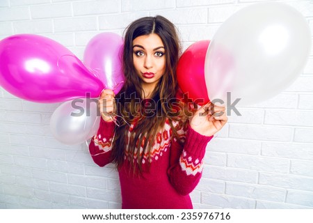 Indoor lifestyle image of funny pretty brunette girl with bright make up and long hairs, wearing trendy sweater and holding pink party balloons. Send positive kiss.