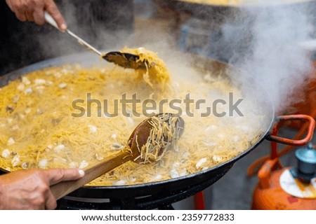 Appetizing racy seafood fideua, noodle paella with mussels, prawns and squid in large paellera. Popular street food during holidays. Traditional Valencian cuisine.. Royalty-Free Stock Photo #2359772833