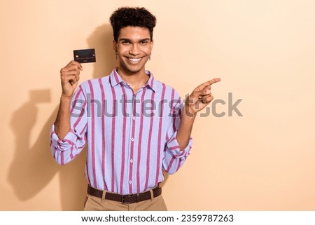 Photo portrait of nice young guy credit card point empty space wear trendy striped formalwear garment isolated on beige color background