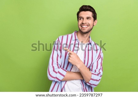 Photo of young friendly calm guy wearing striped shirt pointing finger empty space presentation offer isolated on green color background