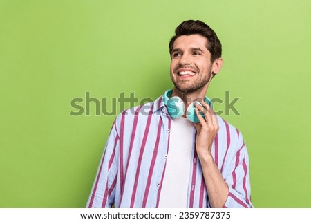 Photo of good mood man dressed striped shirt hold smartphone touch headphones look at promo empty space isolated on green color background Royalty-Free Stock Photo #2359787375