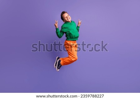 Photo of positive glad boy pupil wear green trendy outfit fly air demonstrate v-sign good mood isolated on purple color background