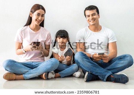 Happy family father and mother with daughter sitting and use technology together of smartphone on wall background