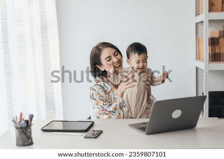 A little boy Asian baby in mother's arms, excited and joyful use computer laptop with video calls with father or long-distance relatives. Tech-Fueled Family Love Concept.