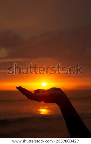 Silhouette of a hand holding the sun, in front of the sea at sun