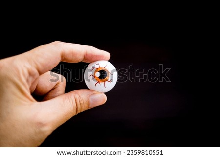 Plastic eyeball toy in girl hand with space on black background, Halloween decoration item Royalty-Free Stock Photo #2359810551