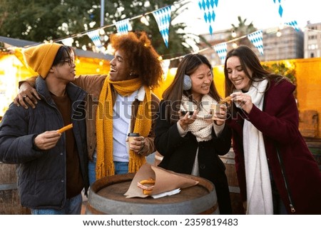 Multiracial friends drinking hot chocolate and eating churros at a winter market.