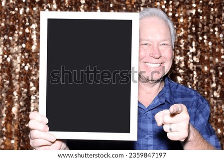 Photo Booth. A smiles as he holds a blank Black sign while having his pictures taken in a Photo Booth. Blank Sign. Room for text or images. Photo Booth Sign. Wedding Photo Booth. Party Time. Fun Times
