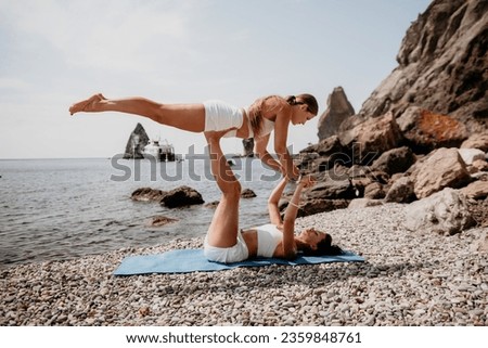 Woman sea yoga. Two Happy women meditating in yoga pose on the beach, ocean and rock mountains. Motivation and inspirational fit and exercising. Healthy lifestyle outdoors in nature, fitness concept.