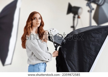 Portrait of beautiful young creative woman photographer working in modern photo studio, Business-savvy woman confidently showcases photo equipment amidst a studio set with lights and camera.