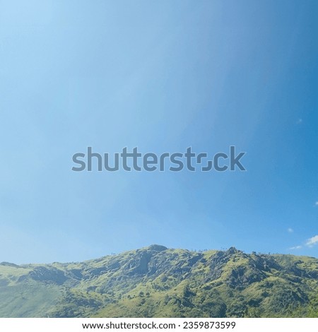 Stunning photograph of a mountainous landscape under a clear blue sky. The photo captures the grandeur of the mountain, which is covered in lush greenery and has a rocky peak.