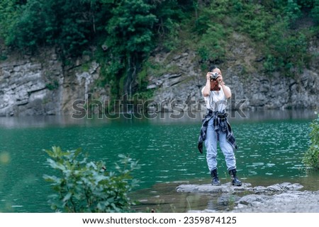 a young adventurer stands on the shore of a lake and uses an analog camera to take pictures of surrounding nature. Asian woman loves taking nature photos on her analog camera as a hobby