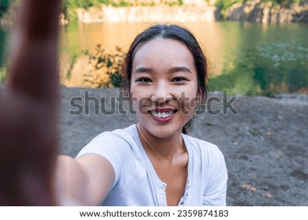a beautiful young hiker uses her phone to take a picture and record her adventure. Young Asian travel vloger uses her phone to document her hiking trip