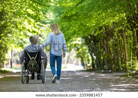 Man in wheelchair walking at park with his wife.