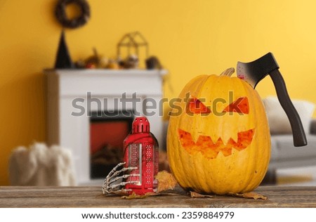 Jack-O-Lantern pumpkin with ax, lantern and leaves on table in room decorated for Halloween party