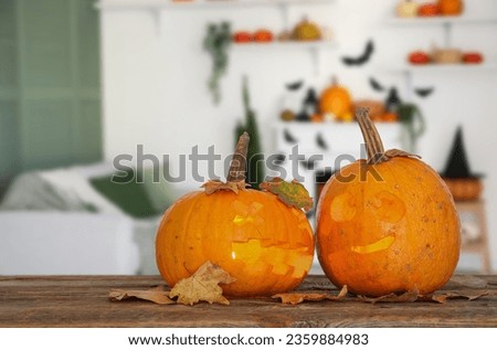 Jack-O-Lantern pumpkins and leaves on table in room decorated for Halloween party