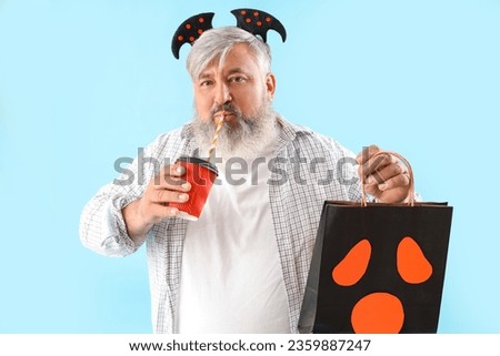 Mature man dressed for Halloween with gift bag drinking on blue background