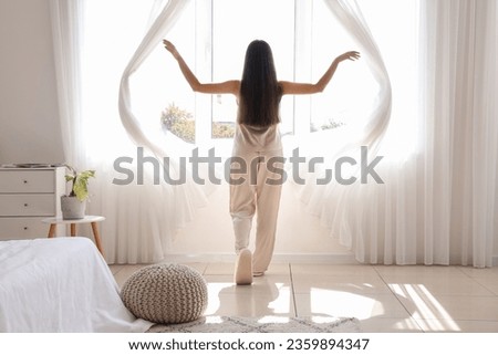 Morning of pretty young woman opening curtains in bedroom Royalty-Free Stock Photo #2359894347