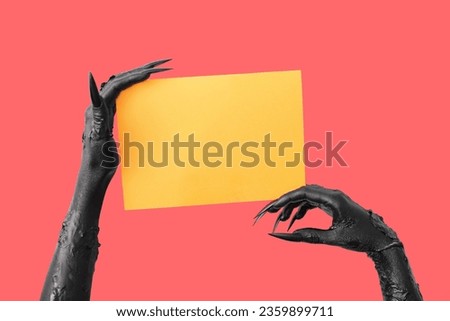 Black hands of witch with blank orange paper sheet on red background. Halloween celebration