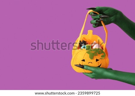Green hands of witch with bag and candies on purple background. Halloween celebration